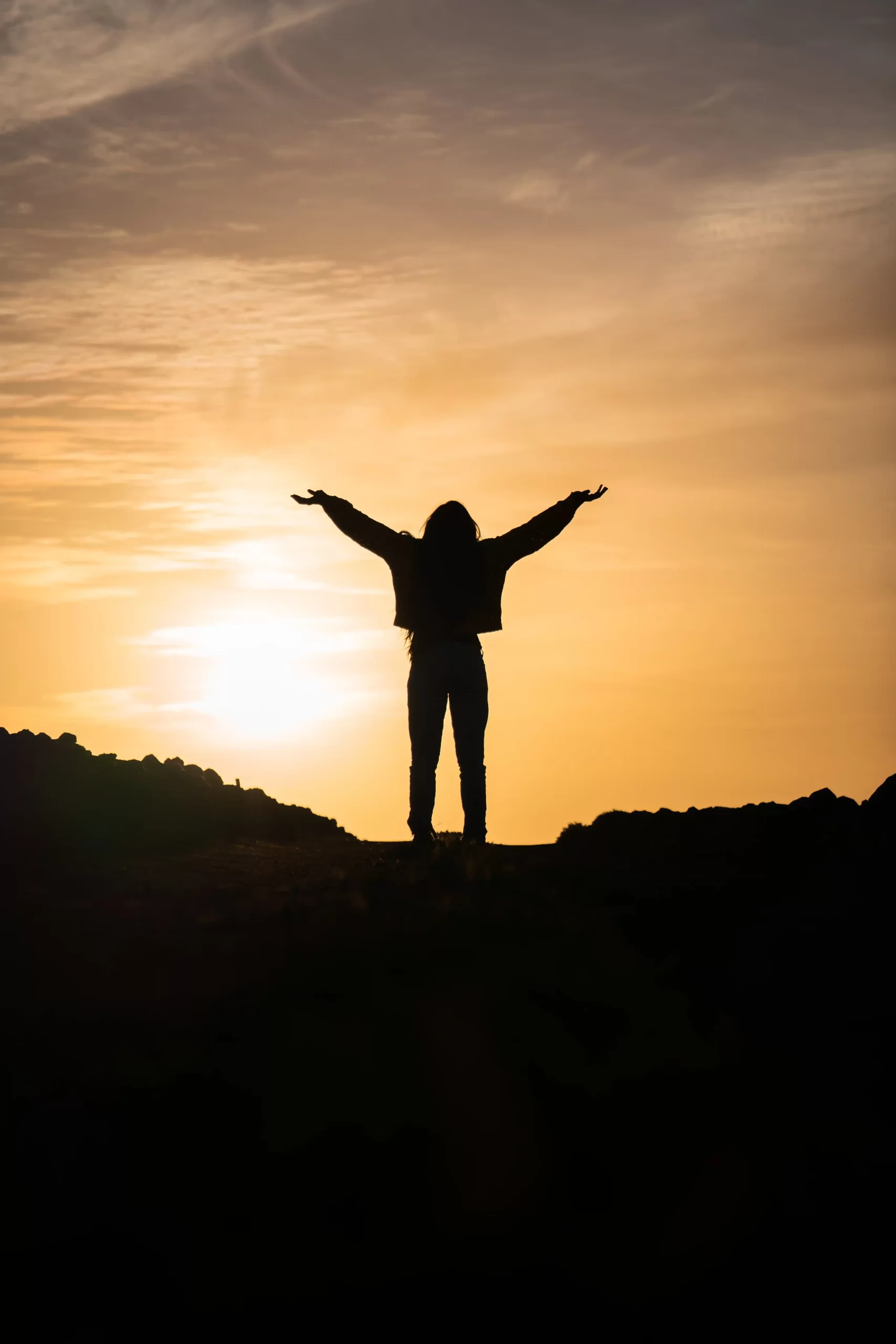 vertical-shot-person-with-hands-up-against-background-sunset